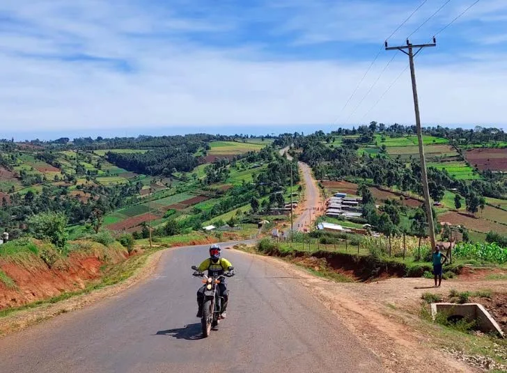 a motorcyclist riding through an East African landscape with agriculture